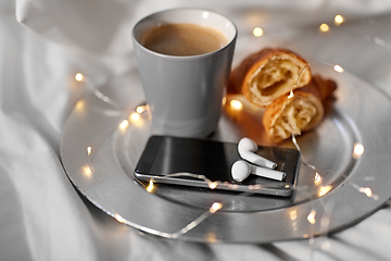 Image showing smartphone, earphones, coffee and croissant in bed