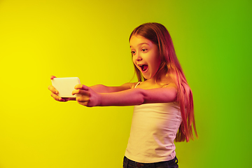 Image showing Little caucasian girl\'s portrait isolated on gradient background in neon light. Concept of human emotions, facial expression, modern gadgets and technologies. Copyspace.