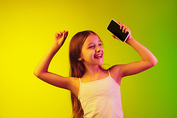 Image showing Little caucasian girl\'s portrait isolated on gradient background in neon light. Concept of human emotions, facial expression, modern gadgets and technologies. Copyspace.