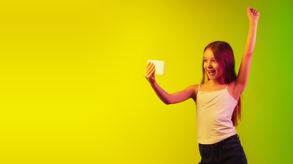Image showing Little caucasian girl\'s portrait isolated on gradient background in neon light. Concept of human emotions, facial expression, modern gadgets and technologies. Copyspace.