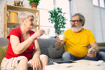 Image showing Couple of seniors spending time together being quarantined - caucasians mature and retired man and woman using modern gadgets, talking, drinking tea