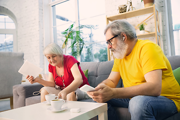 Image showing Couple of seniors spending time together being quarantined - caucasians mature and retired man and woman using modern gadgets, talking, drinking tea