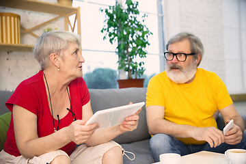 Image showing Couple of seniors spending time together being quarantined - caucasians mature and retired man and woman using modern gadgets, talking, drinking tea