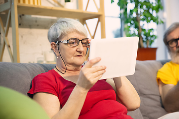 Image showing Couple of seniors spending time together being quarantined - caucasians mature and retired man and woman using modern gadgets, talking, drinking tea