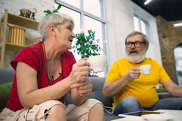 Image showing Couple of seniors spending time together being quarantined - caucasians mature and retired man and woman using modern gadgets, talking, drinking tea