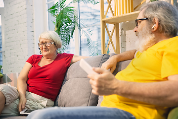 Image showing Couple of seniors spending time together being quarantined - caucasians mature and retired man and woman using modern gadgets, talking, drinking tea