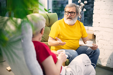 Image showing Couple of seniors spending time together being quarantined - caucasians mature and retired man and woman using modern gadgets, talking, drinking tea