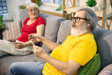Image showing Couple of seniors spending time together being quarantined - caucasians mature and retired man and woman using modern gadgets, talking, drinking tea