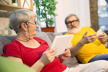 Image showing Couple of seniors spending time together being quarantined - caucasians mature and retired man and woman using modern gadgets, talking, drinking tea