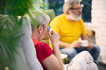 Image showing Couple of seniors spending time together being quarantined - caucasians mature and retired man and woman using modern gadgets, talking, drinking tea