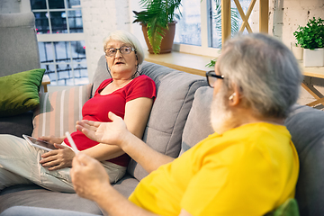 Image showing Couple of seniors spending time together being quarantined - caucasians mature and retired man and woman using modern gadgets, talking, drinking tea