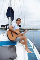 Image showing Young cheerful man playing guitar at boat party outdoor, smiling and happy