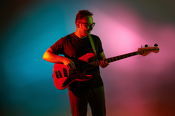 Image showing Young caucasian musician playing on gradient background in neon light. Concept of music, hobby, festival