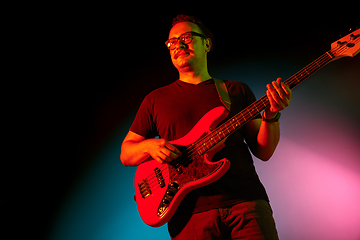 Image showing Young caucasian musician playing on gradient background in neon light. Concept of music, hobby, festival