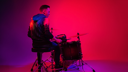 Image showing Young caucasian musician playing on gradient background in neon light. Concept of music, hobby, festival