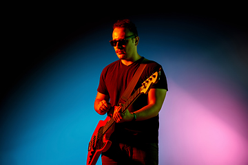 Image showing Young caucasian musician playing on gradient background in neon light. Concept of music, hobby, festival