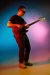 Image showing Young caucasian musician playing on gradient background in neon light. Concept of music, hobby, festival