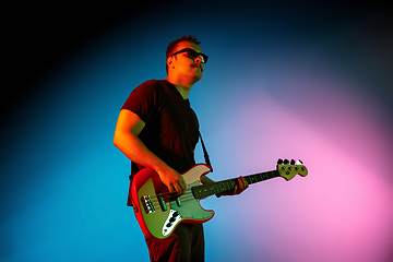 Image showing Young caucasian musician playing on gradient background in neon light. Concept of music, hobby, festival