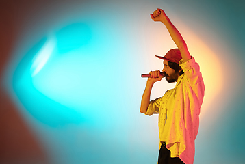 Image showing Young caucasian musician playing, singing on gradient background in neon light. Concept of music, hobby, festival