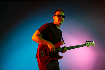 Image showing Young caucasian musician playing on gradient background in neon light. Concept of music, hobby, festival