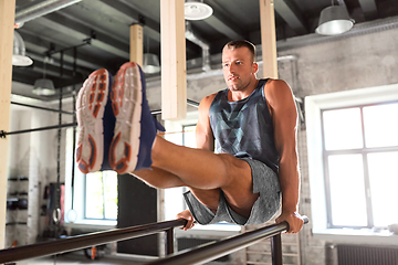 Image showing man flexing abs on parallel bars in gym