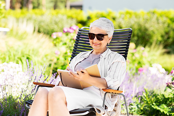 Image showing happy senior woman with diary at summer garden