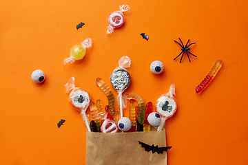 Image showing halloween sweets in paper bag on orange background