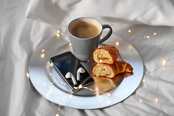Image showing smartphone, earphones, coffee and croissant in bed