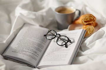 Image showing croissants, cup of coffee and book in bed at home