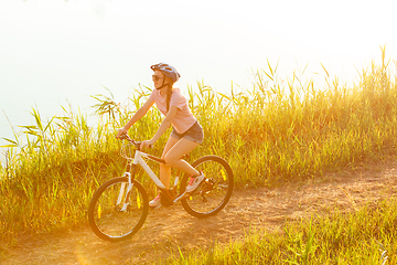 Image showing Joyful young woman riding a bicycle at the riverside and meadow promenade