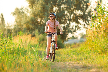 Image showing Joyful young woman riding a bicycle at the riverside and meadow promenade