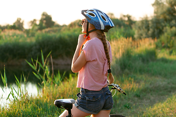 Image showing Joyful young woman riding a bicycle at the riverside and meadow promenade