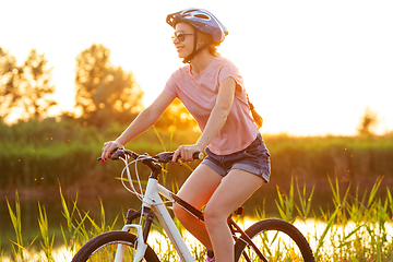 Image showing Joyful young woman riding a bicycle at the riverside and meadow promenade