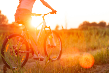 Image showing Joyful young woman riding a bicycle at the riverside and meadow promenade