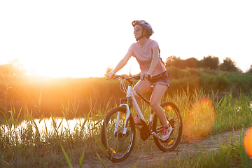 Image showing Joyful young woman riding a bicycle at the riverside and meadow promenade