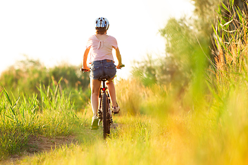 Image showing Joyful young woman riding a bicycle at the riverside and meadow promenade