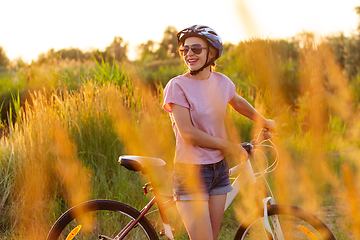 Image showing Joyful young woman riding a bicycle at the riverside and meadow promenade