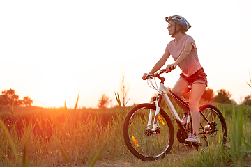 Image showing Joyful young woman riding a bicycle at the riverside and meadow promenade