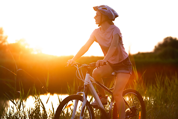 Image showing Joyful young woman riding a bicycle at the riverside and meadow promenade