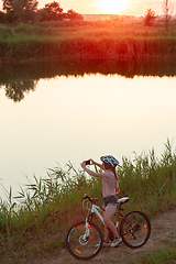 Image showing Joyful young woman riding a bicycle at the riverside and meadow promenade
