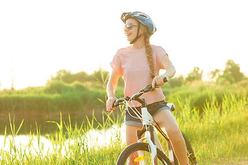 Image showing Joyful young woman riding a bicycle at the riverside and meadow promenade