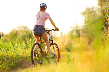 Image showing Joyful young woman riding a bicycle at the riverside and meadow promenade