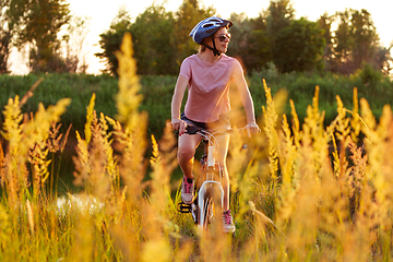 Image showing Joyful young woman riding a bicycle at the riverside and meadow promenade