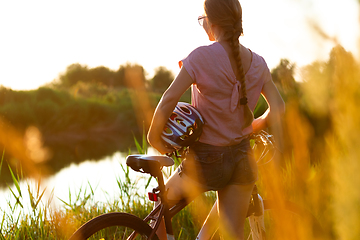 Image showing Joyful young woman riding a bicycle at the riverside and meadow promenade