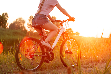 Image showing Joyful young woman riding a bicycle at the riverside and meadow promenade