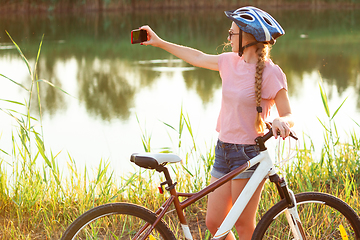 Image showing Joyful young woman riding a bicycle at the riverside and meadow promenade
