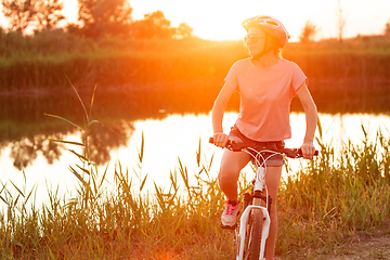 Image showing Joyful young woman riding a bicycle at the riverside and meadow promenade