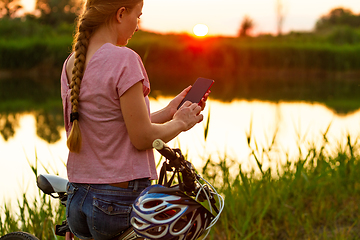 Image showing Joyful young woman riding a bicycle at the riverside and meadow promenade