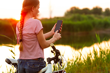 Image showing Joyful young woman riding a bicycle at the riverside and meadow promenade