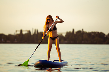 Image showing Young attractive woman standing on paddle board, SUP. Active life, sport, leisure activity concept